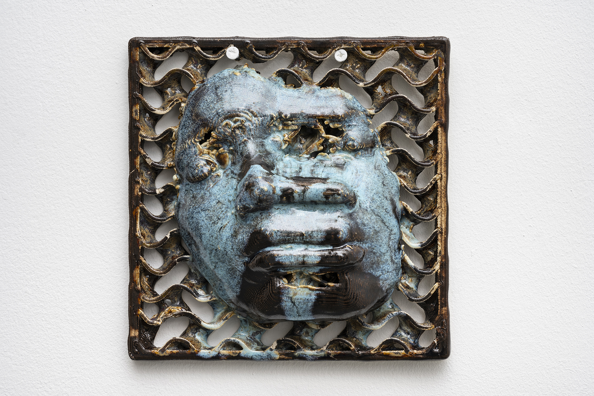 blue and brown 3D printed ceramic piece showing a glitched face with closed eyes in the center, surrounded by wave-like patterns on a white background