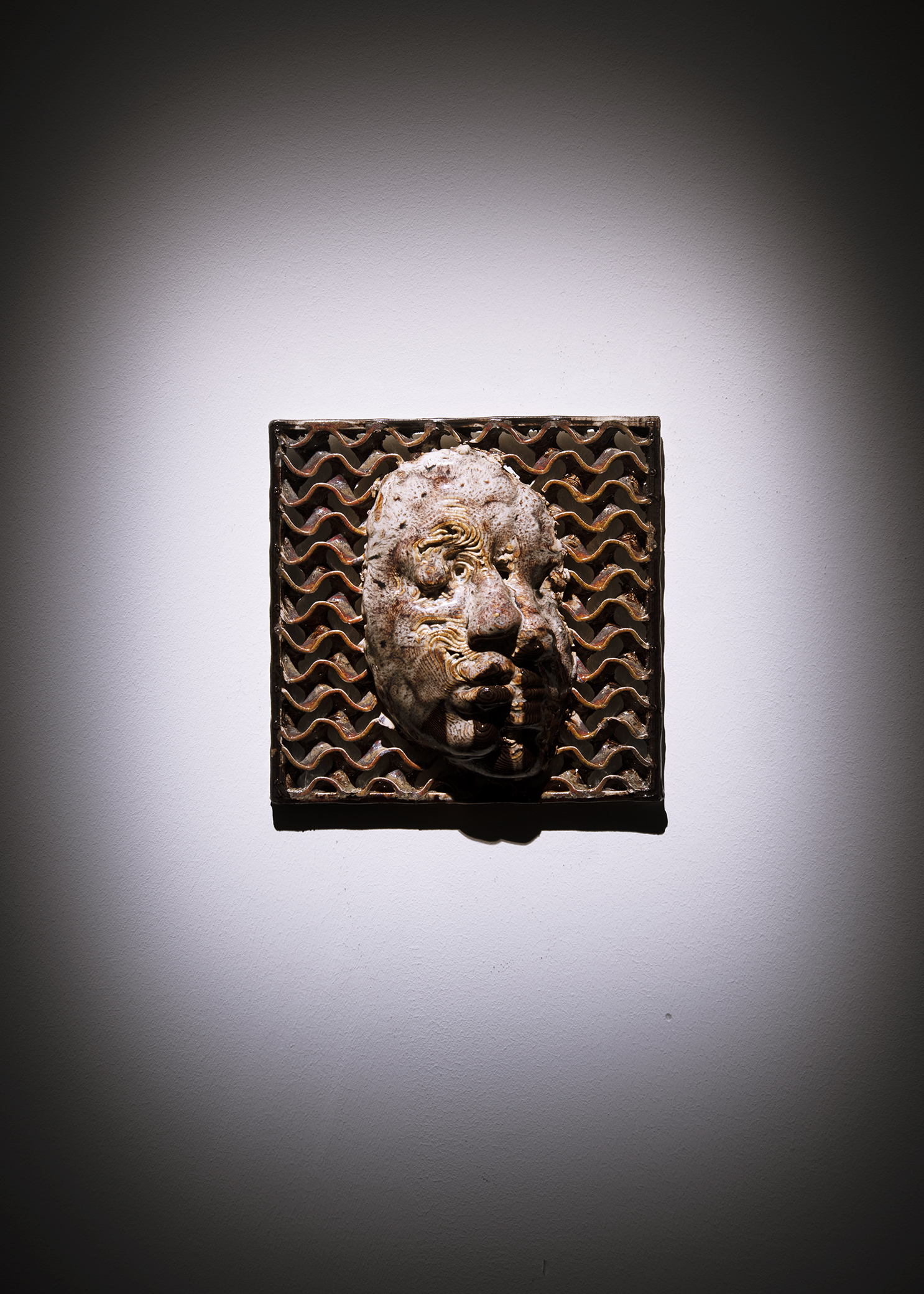 Wall-based brown ceramic piece hung on a wall, showing a face with their eyes closed and right half slightly glitched.