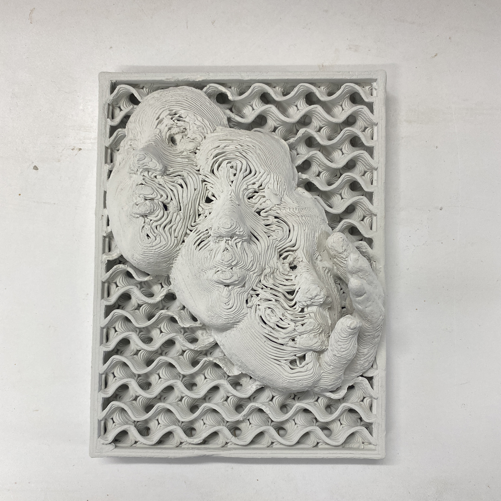photo of a white, unfired ceramic piece with a square frame around it, three faces blended together and a hand on the right side